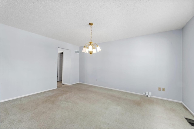 spare room with an inviting chandelier, carpet flooring, visible vents, and a textured ceiling