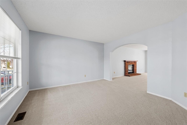 carpeted empty room featuring arched walkways, visible vents, a brick fireplace, and a textured ceiling