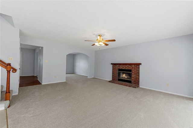 unfurnished living room with a brick fireplace, carpet flooring, a ceiling fan, and arched walkways