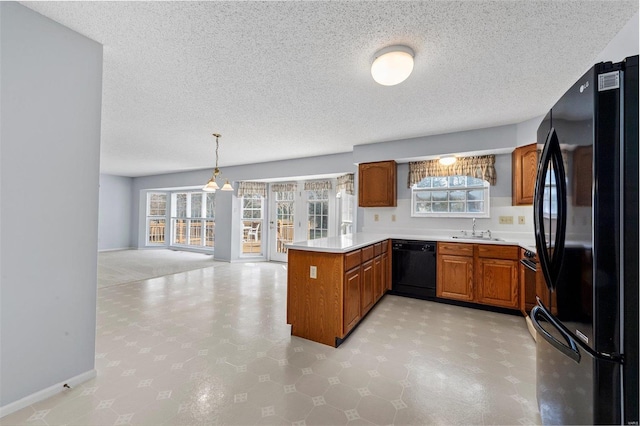 kitchen with light countertops, a peninsula, brown cabinetry, black appliances, and a sink