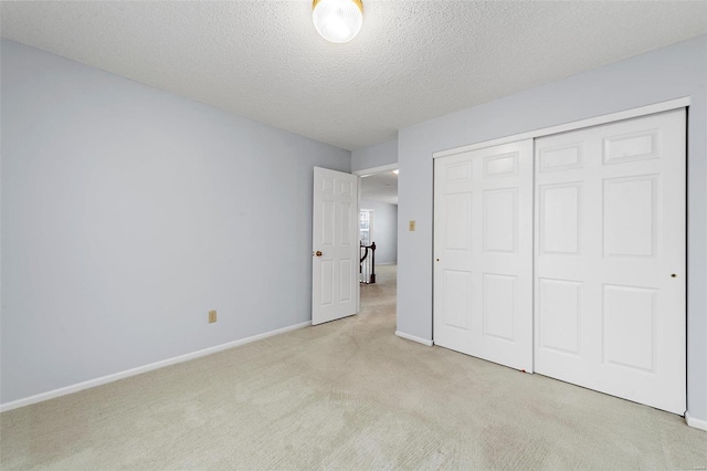 unfurnished bedroom featuring a textured ceiling, baseboards, a closet, and light carpet