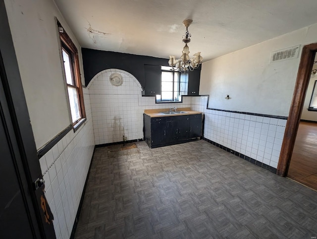 kitchen with visible vents, a sink, dark cabinetry, tile walls, and a chandelier