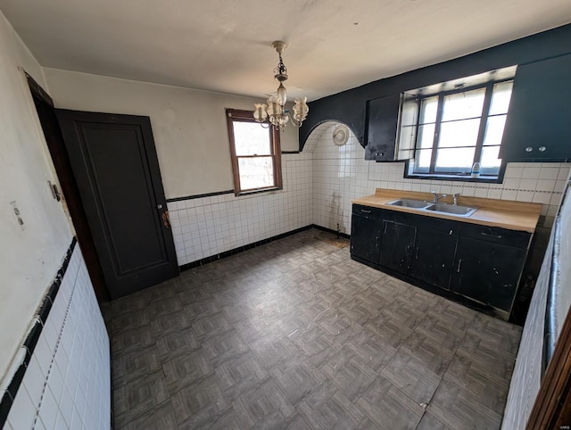 kitchen featuring a chandelier, dark cabinetry, tile walls, wood counters, and a sink