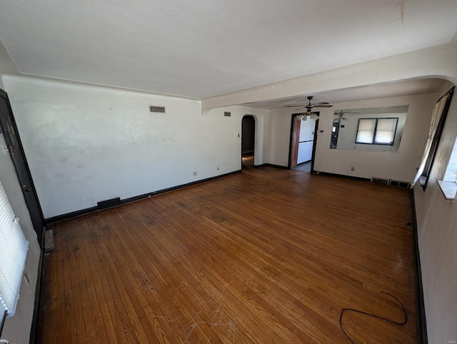 empty room with visible vents, a ceiling fan, arched walkways, baseboards, and dark wood-style flooring