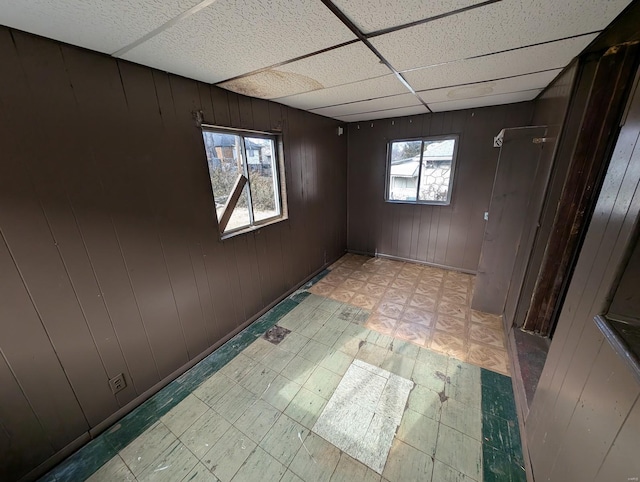 empty room with a paneled ceiling, light floors, and wood walls