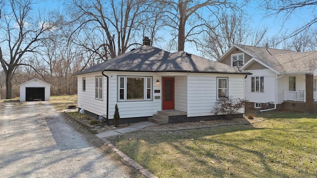 view of front facade featuring a detached garage, a front lawn, a chimney, an outbuilding, and driveway