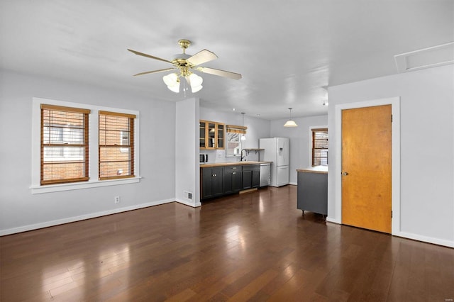 unfurnished living room featuring a ceiling fan, plenty of natural light, dark wood-style floors, and a sink