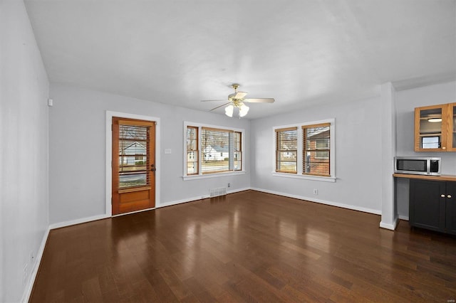 unfurnished living room featuring visible vents, baseboards, dark wood-style floors, and a ceiling fan