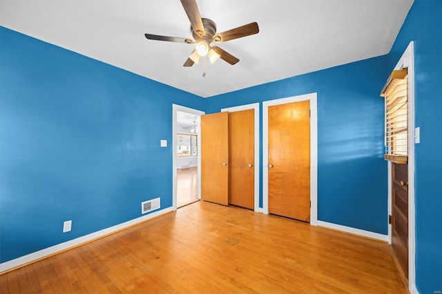 unfurnished bedroom with visible vents, wood finished floors, multiple closets, and baseboards