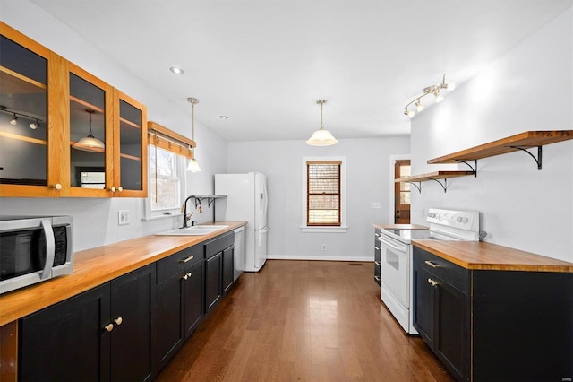 kitchen with a sink, white appliances, wooden counters, and dark cabinets