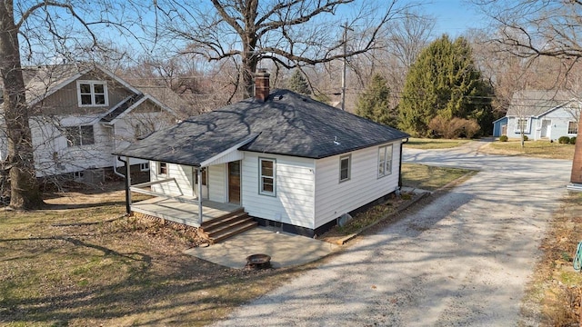 exterior space featuring a shingled roof, a porch, driveway, and a chimney