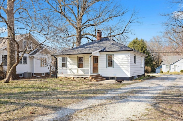 bungalow with a porch, central AC, gravel driveway, a front yard, and a chimney