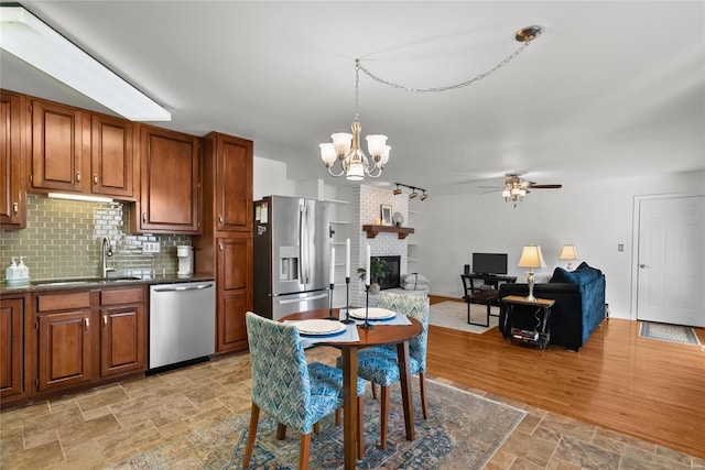 kitchen with a sink, appliances with stainless steel finishes, stone finish flooring, ceiling fan with notable chandelier, and tasteful backsplash