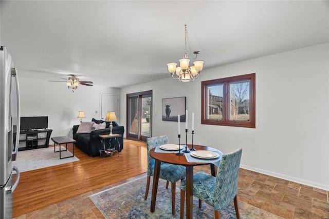 dining room featuring baseboards, ceiling fan with notable chandelier, and stone finish floor