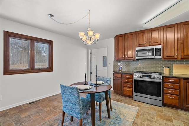 kitchen with backsplash, stone finish flooring, baseboards, a chandelier, and appliances with stainless steel finishes