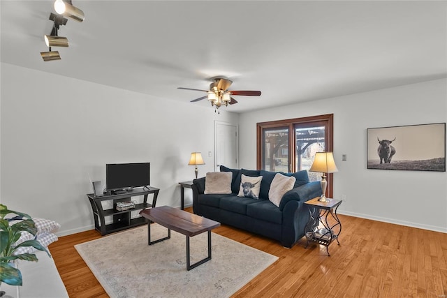 living room featuring baseboards, a ceiling fan, and light wood finished floors