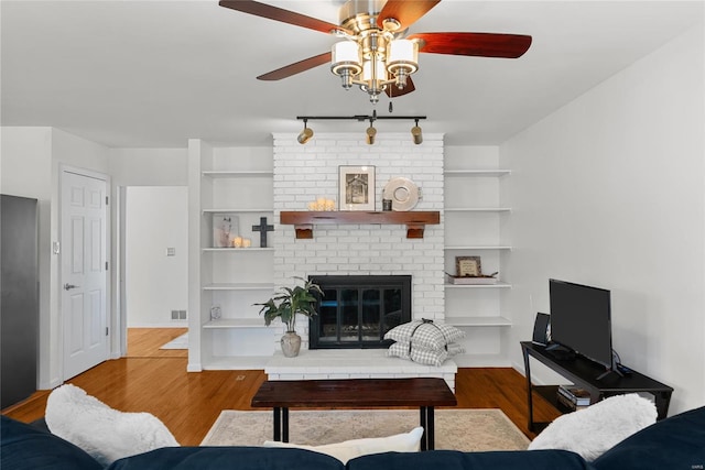 living room with wood finished floors, built in shelves, a ceiling fan, and visible vents