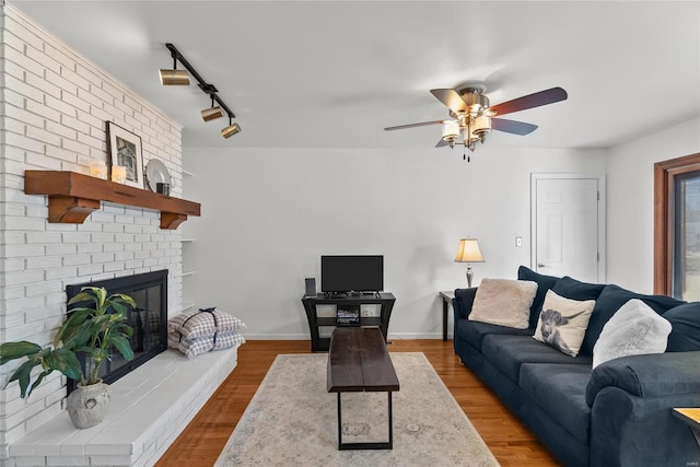 living area with a brick fireplace, baseboards, a ceiling fan, and wood finished floors