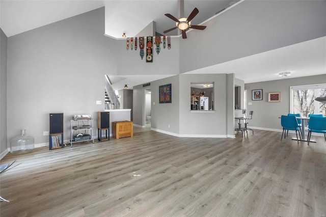 unfurnished living room with wood finished floors, stairway, a ceiling fan, and baseboards