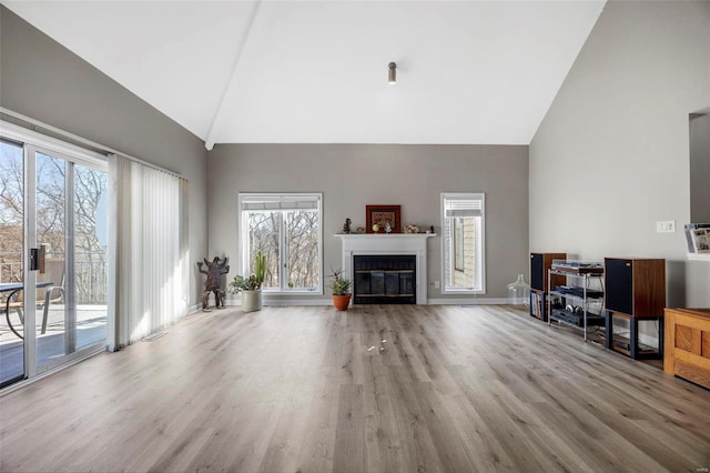 living room featuring a glass covered fireplace, baseboards, high vaulted ceiling, and wood finished floors