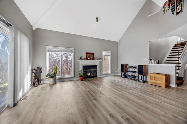 unfurnished living room with a glass covered fireplace, stairway, wood finished floors, and high vaulted ceiling