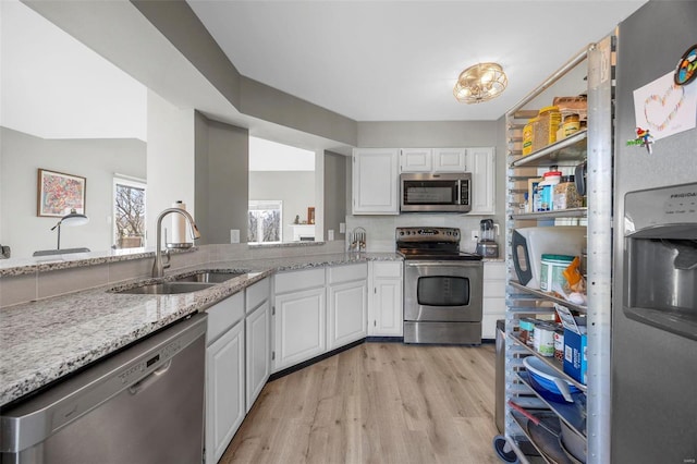 kitchen with light stone counters, light wood finished floors, a sink, appliances with stainless steel finishes, and white cabinetry