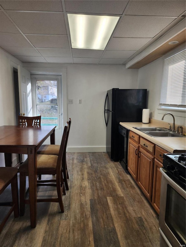 kitchen with brown cabinets, a sink, black dishwasher, dark wood finished floors, and stainless steel range with gas cooktop