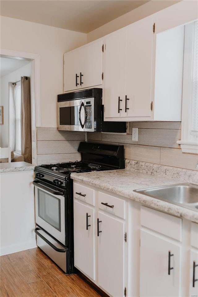 kitchen with stainless steel microwave, light countertops, gas range oven, decorative backsplash, and white cabinets