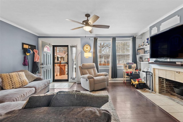 living room featuring a tiled fireplace, wood finished floors, a ceiling fan, and ornamental molding