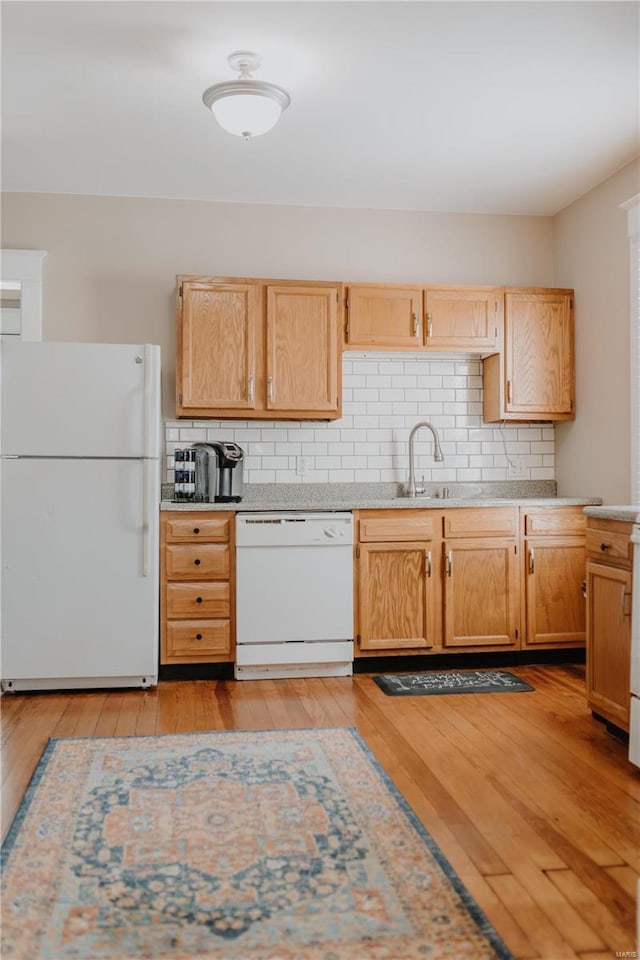 kitchen featuring white appliances, light wood finished floors, a sink, light countertops, and tasteful backsplash