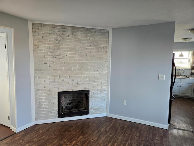 unfurnished living room featuring a sink, baseboards, a fireplace, and dark wood-style flooring