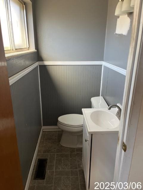 half bathroom with visible vents, wainscoting, vanity, and toilet