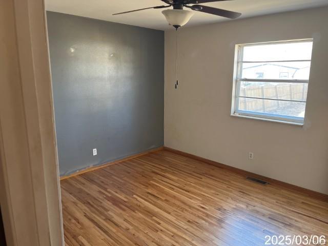 spare room featuring visible vents, wood finished floors, baseboards, and ceiling fan