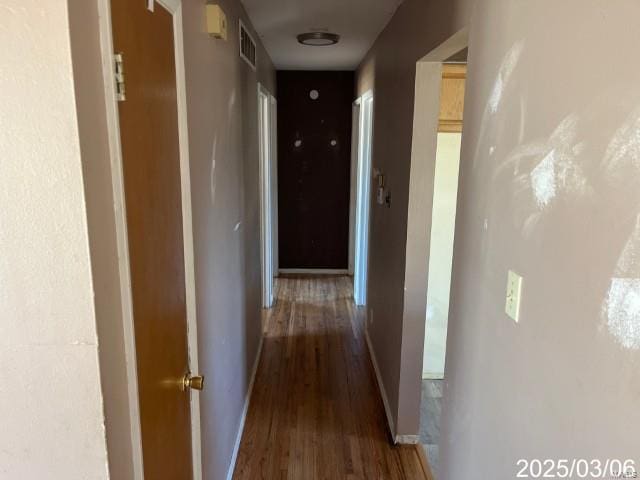 corridor featuring visible vents, baseboards, and wood finished floors