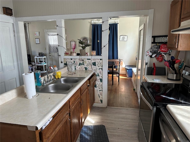 kitchen featuring light countertops, light wood-type flooring, brown cabinets, stainless steel range with electric cooktop, and a sink