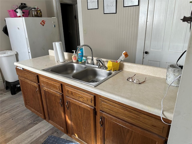 kitchen with light wood-type flooring, brown cabinets, a sink, freestanding refrigerator, and light countertops