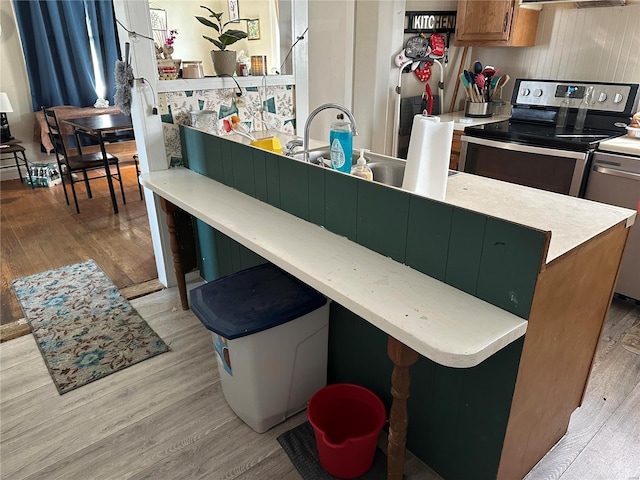 kitchen with a sink, light wood-style floors, stainless steel range with electric stovetop, and light countertops