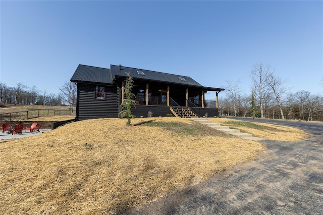 view of front facade featuring a porch, metal roof, a front yard, and fence