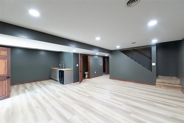 finished basement with stairway, light wood-style flooring, visible vents, and a sink