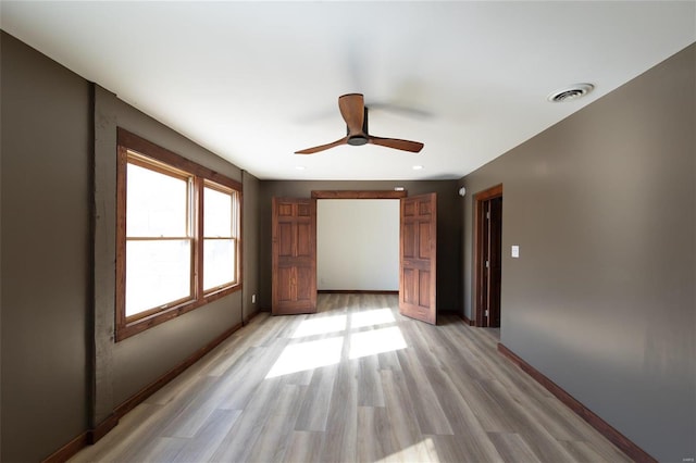 spare room featuring light wood finished floors, visible vents, ceiling fan, and baseboards