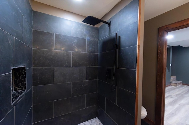 bathroom with toilet, wood finished floors, and tiled shower