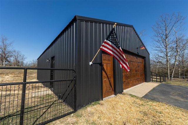 view of outdoor structure with aphalt driveway, fence, a garage, and an outdoor structure