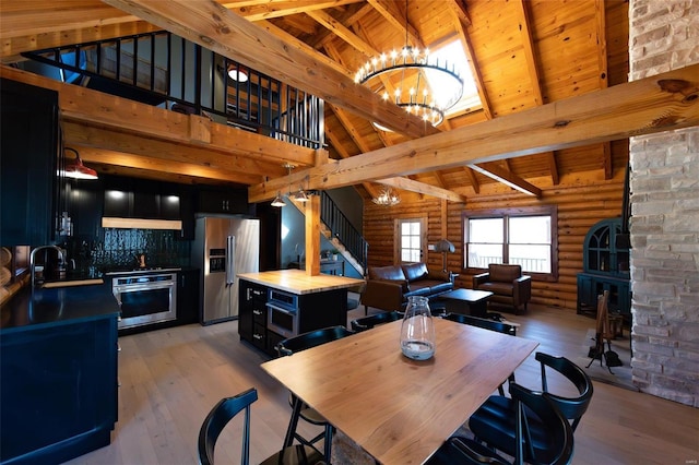 dining space featuring light wood-type flooring, beamed ceiling, high vaulted ceiling, a fireplace, and stairs