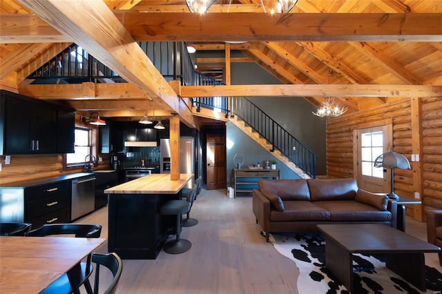 living room with stairway, beamed ceiling, light wood-style flooring, plenty of natural light, and high vaulted ceiling