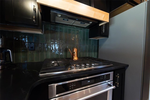 kitchen with dark countertops, range hood, stainless steel appliances, decorative backsplash, and dark cabinets