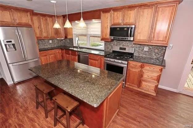 kitchen featuring dark wood-style floors, a breakfast bar, decorative backsplash, appliances with stainless steel finishes, and brown cabinets