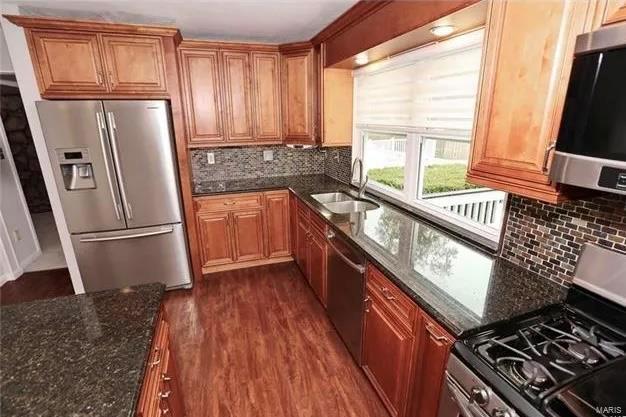 kitchen with a sink, dark wood-style floors, dark stone counters, appliances with stainless steel finishes, and brown cabinetry