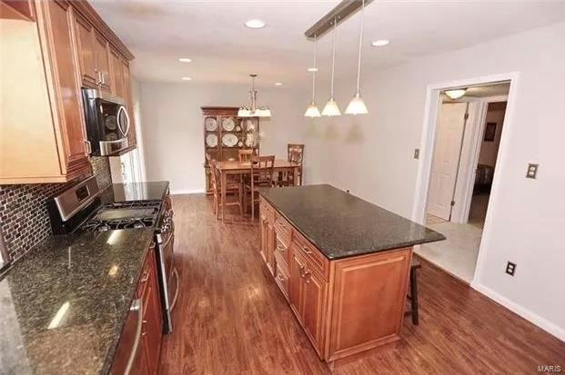 kitchen with dark wood-type flooring, a breakfast bar, tasteful backsplash, stainless steel appliances, and brown cabinetry