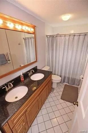 full bath with a sink, toilet, double vanity, and tile patterned floors