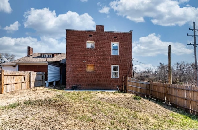 back of property with brick siding, a fenced backyard, and a lawn